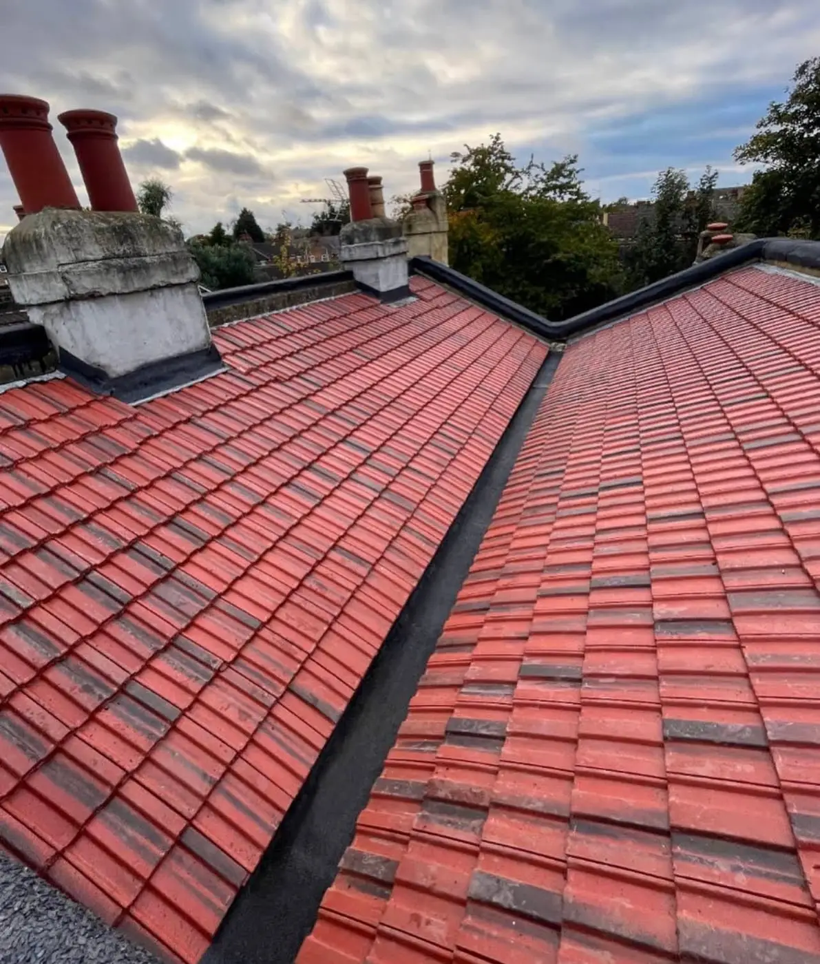 Clay tiled roof slopes meeting at a valley between chimney stacks in London