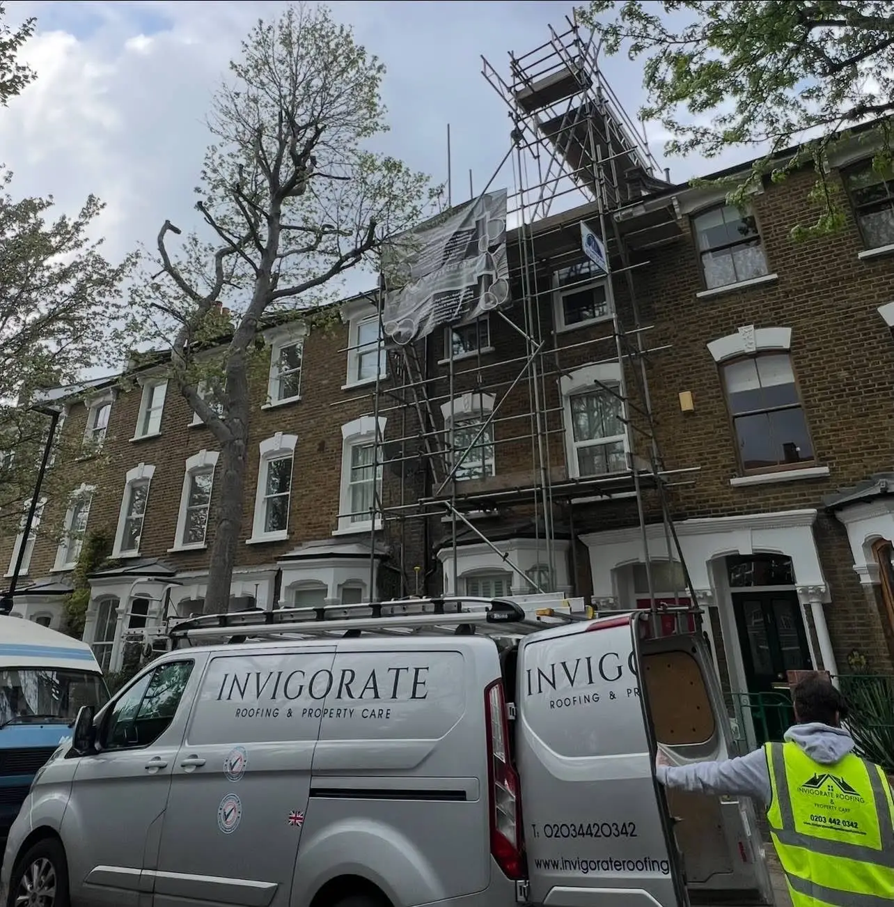 Two Invigorate Roofing vans and a team member outside a scaffolded London terrace