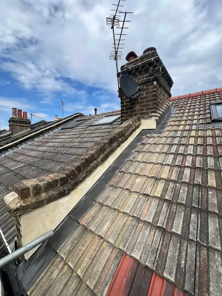 Weathered clay tiled roof with chimney stacks and ridge on a London terrace
